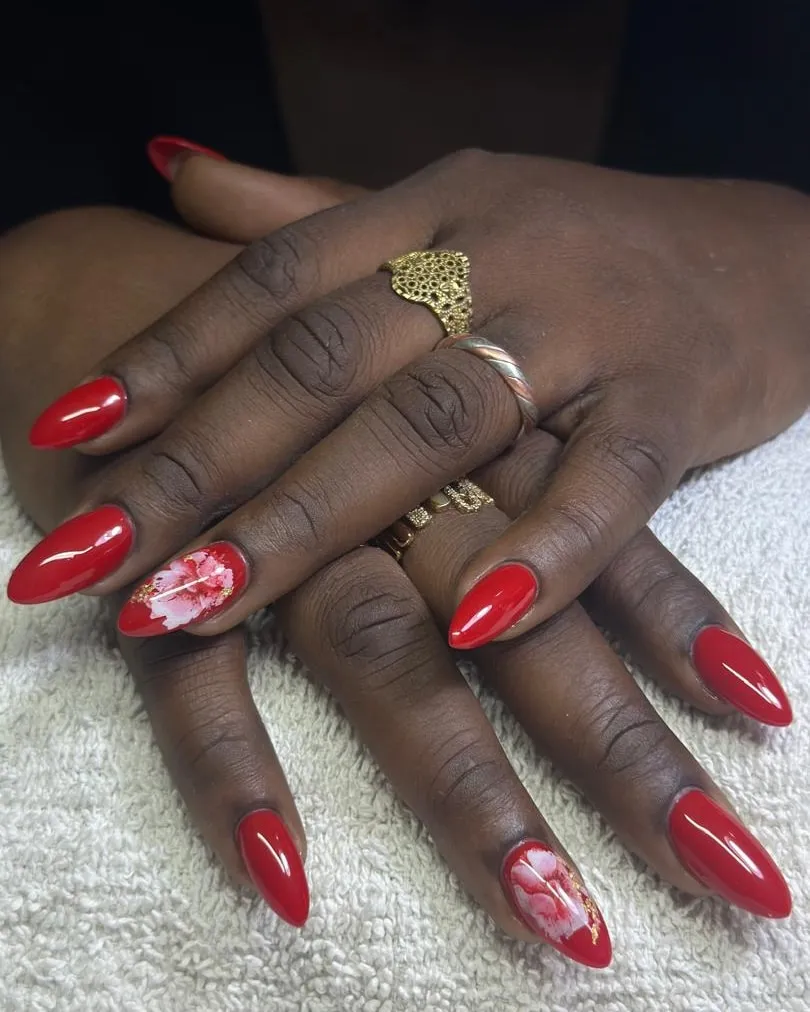 Deux mains croisées, ongles rouges en amande dont deux à motif fleuri blanc, bagues dorées