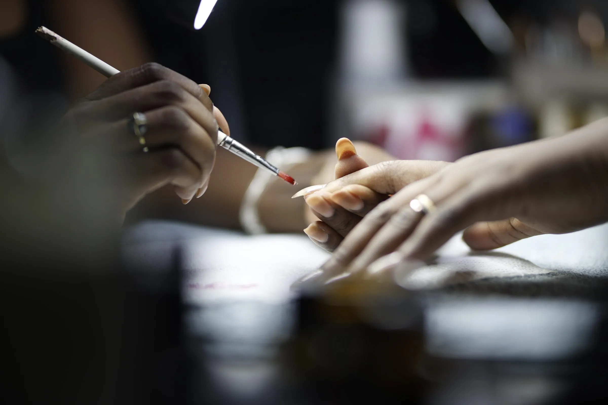 Séance en atelier : une apprenante applique le vernis au pinceau sur la main d'une cliente, autour de la table de travail