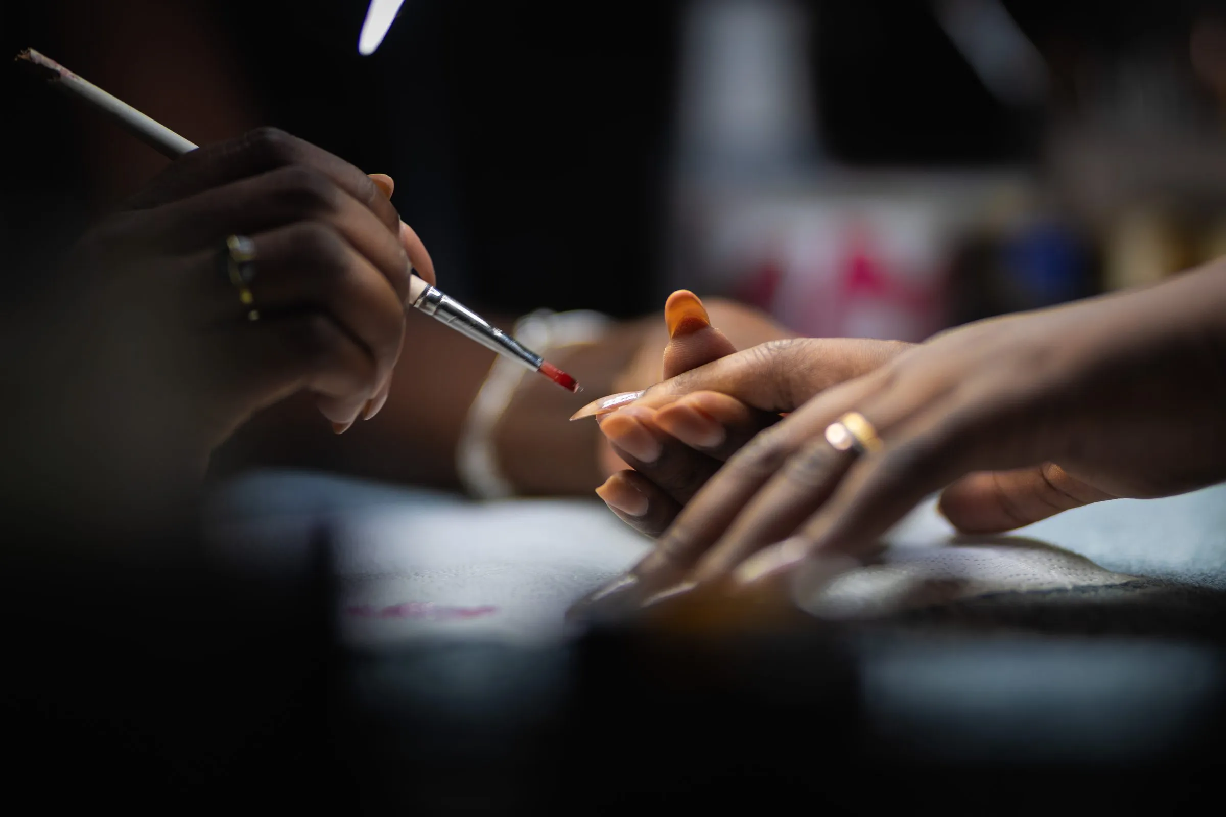 Séance en atelier : une apprenante applique le vernis au pinceau sur la main d'une cliente, autour de la table de travail