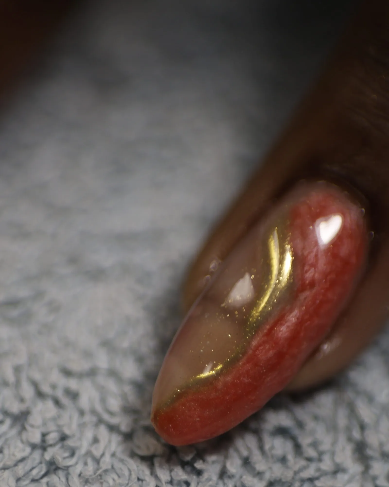 Gros plan d'un ongle en amande rouge corail orné d'une ligne de feuille d'or